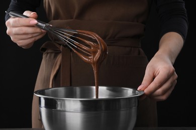 Photo of Woman with whisk mixing chocolate cream on black background, closeup
