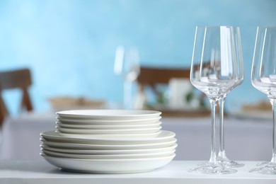 Stacked clean dishes and glasses on white shelf indoors