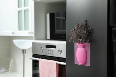 Silicone vase with beautiful violet flowers on fridge in kitchen, space for text