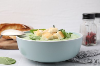 Photo of Delicious spinach cream soup with croutons in bowl on white tiled table