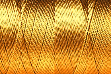 Image of Spool of golden sewing thread as background, closeup