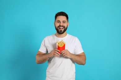 Young man with French fries on light blue background