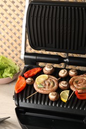 Electric grill with homemade sausages, bell pepper and mushrooms on table, closeup