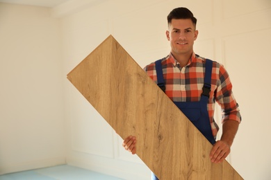 Photo of Professional worker with wooden board indoors. Installing of parquet flooring