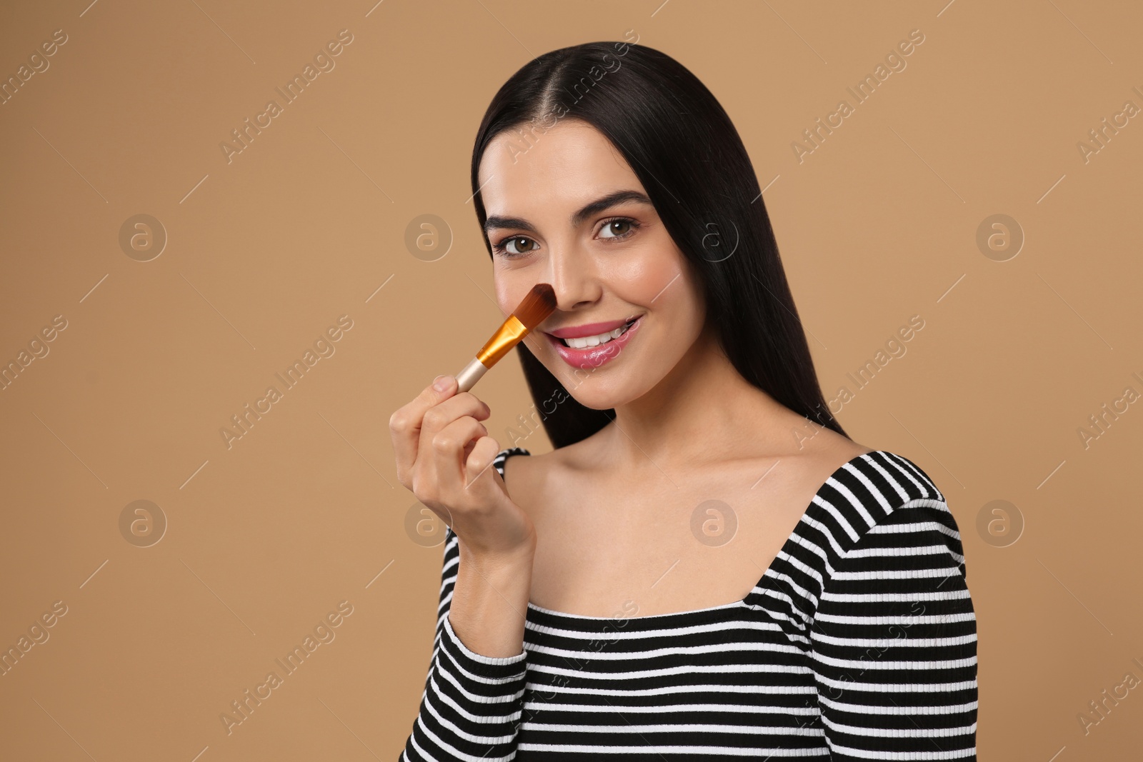 Photo of Beautiful woman applying makeup on light brown background. Space for text