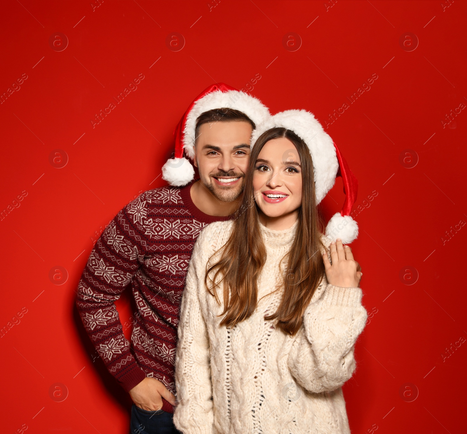 Photo of Couple wearing Christmas sweaters and Santa hats on red background