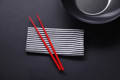 Empty iron wok and chopsticks on black table, flat lay