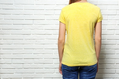 Photo of Back view of young woman wearing blank t-shirt near white brick wall, closeup. Mockup for design