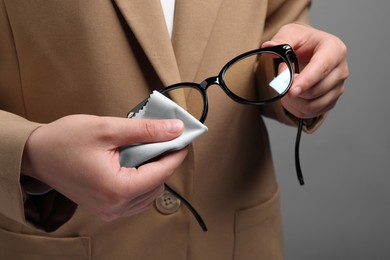 Photo of Woman wiping her glasses with microfiber cloth on grey background, closeup