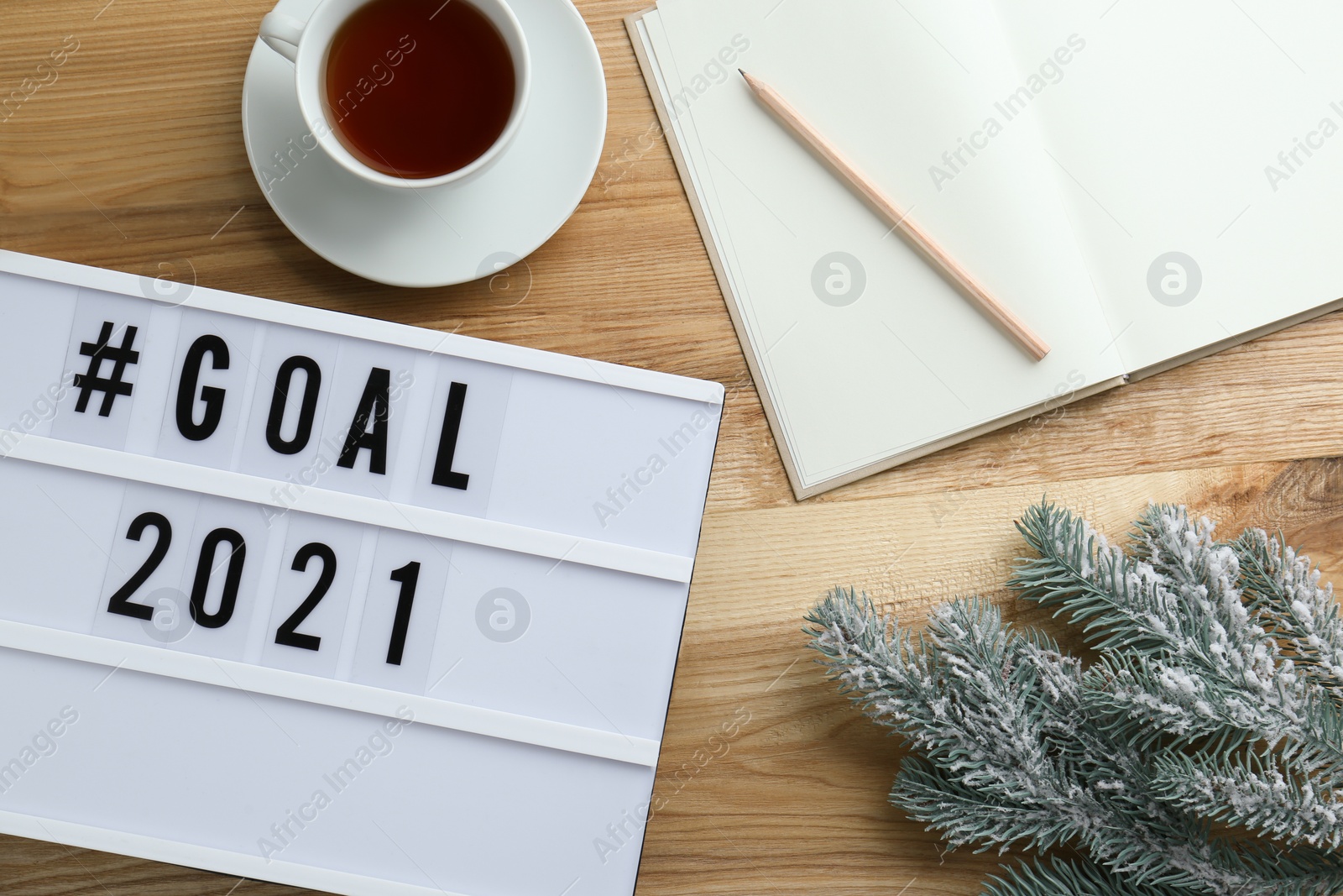 Photo of Light box with hashtag Goal 2021 near notebook, new year targets. Flat lay composition on wooden table