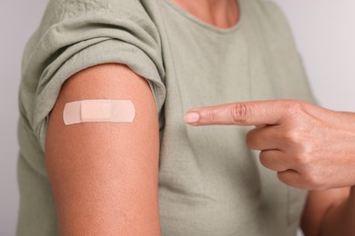 Photo of Woman pointing at adhesive bandage after vaccination on light grey background, closeup