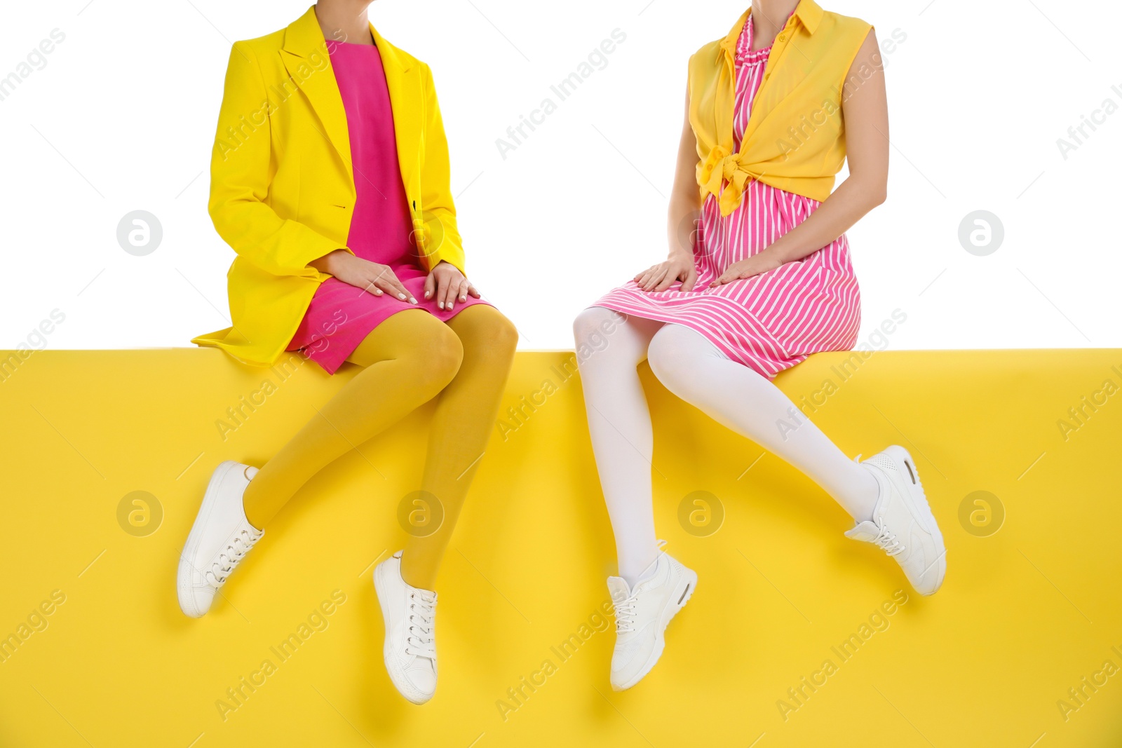 Photo of Women wearing bright tights sitting on color background, closeup