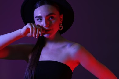 Photo of Portrait of beautiful young woman in hat on color background with neon lights