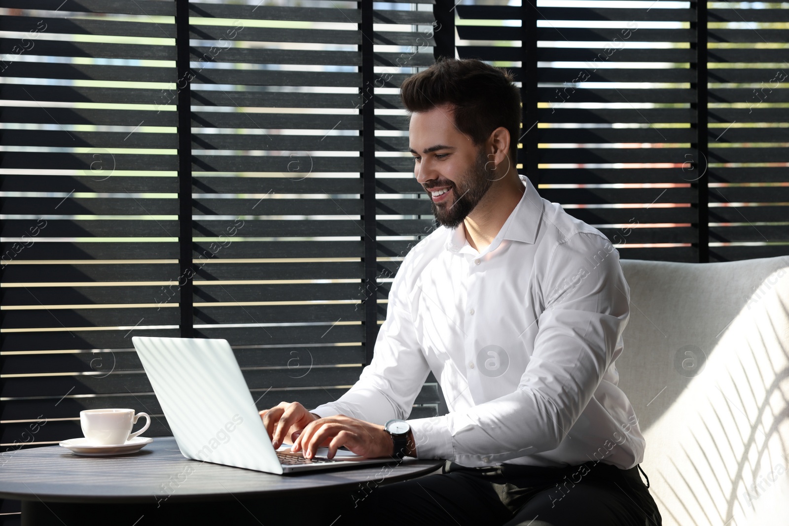 Photo of Happy young man working on laptop at table in office