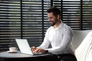 Happy young man working on laptop at table in office