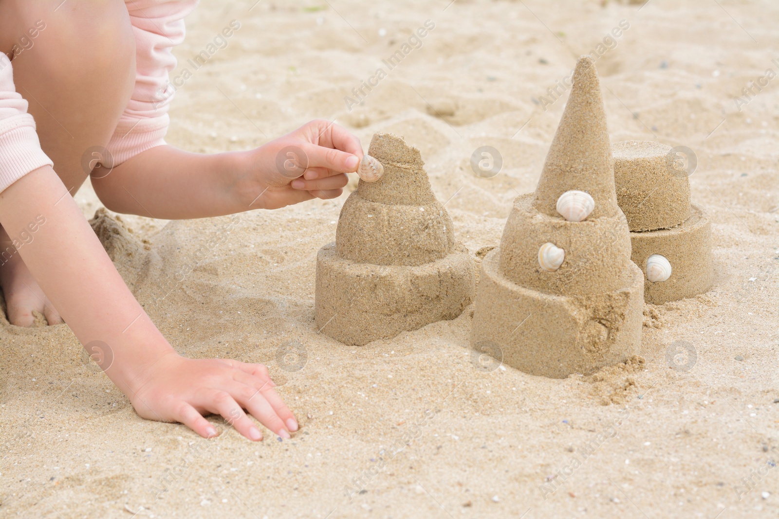 Photo of Child decorating sand castle with shell on beach, closeup