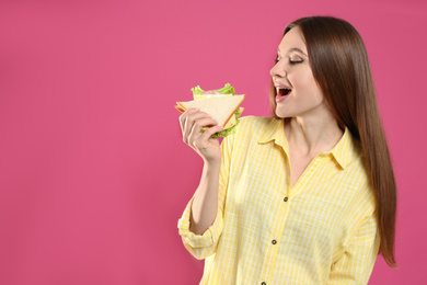 Young woman eating tasty sandwich on pink background