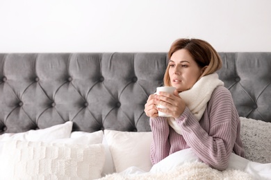 Photo of Sick woman with cup of hot drink suffering from cold in bed