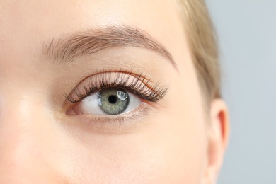 Young woman with beautiful long eyelashes on gray background, closeup. Extension procedure