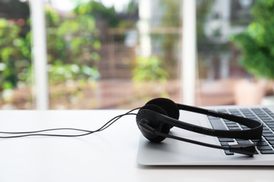 Photo of Modern laptop and headset on table indoors. Technical support concept