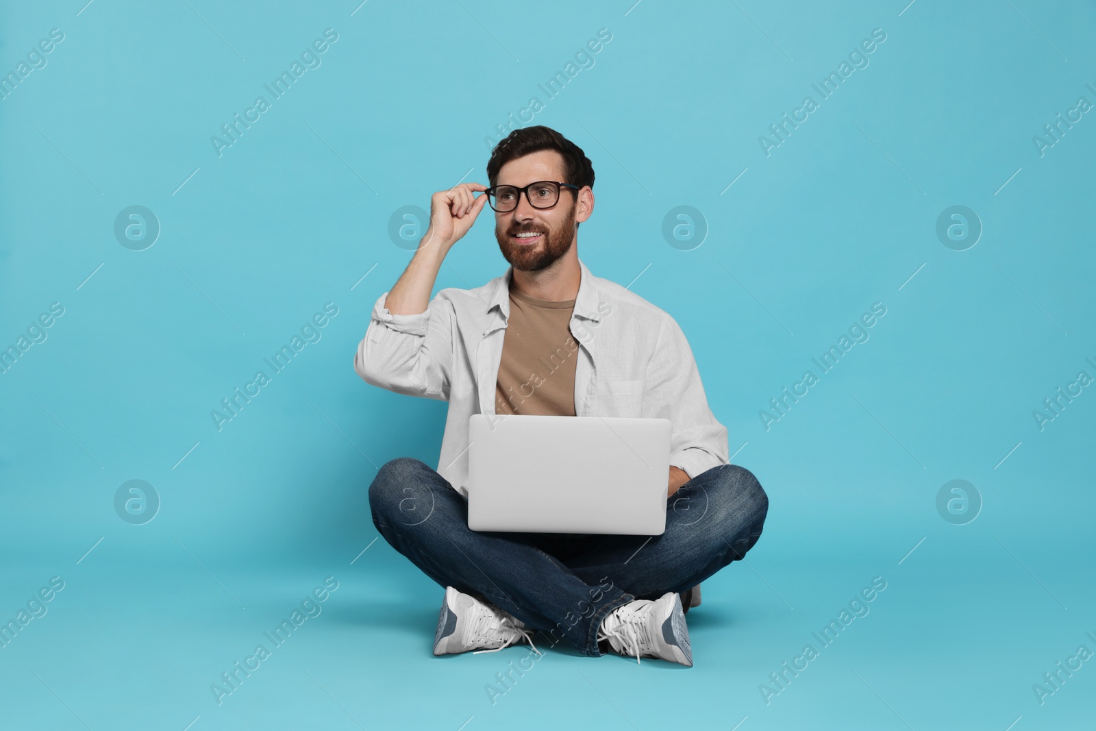 Photo of Handsome man with laptop sitting on light blue background