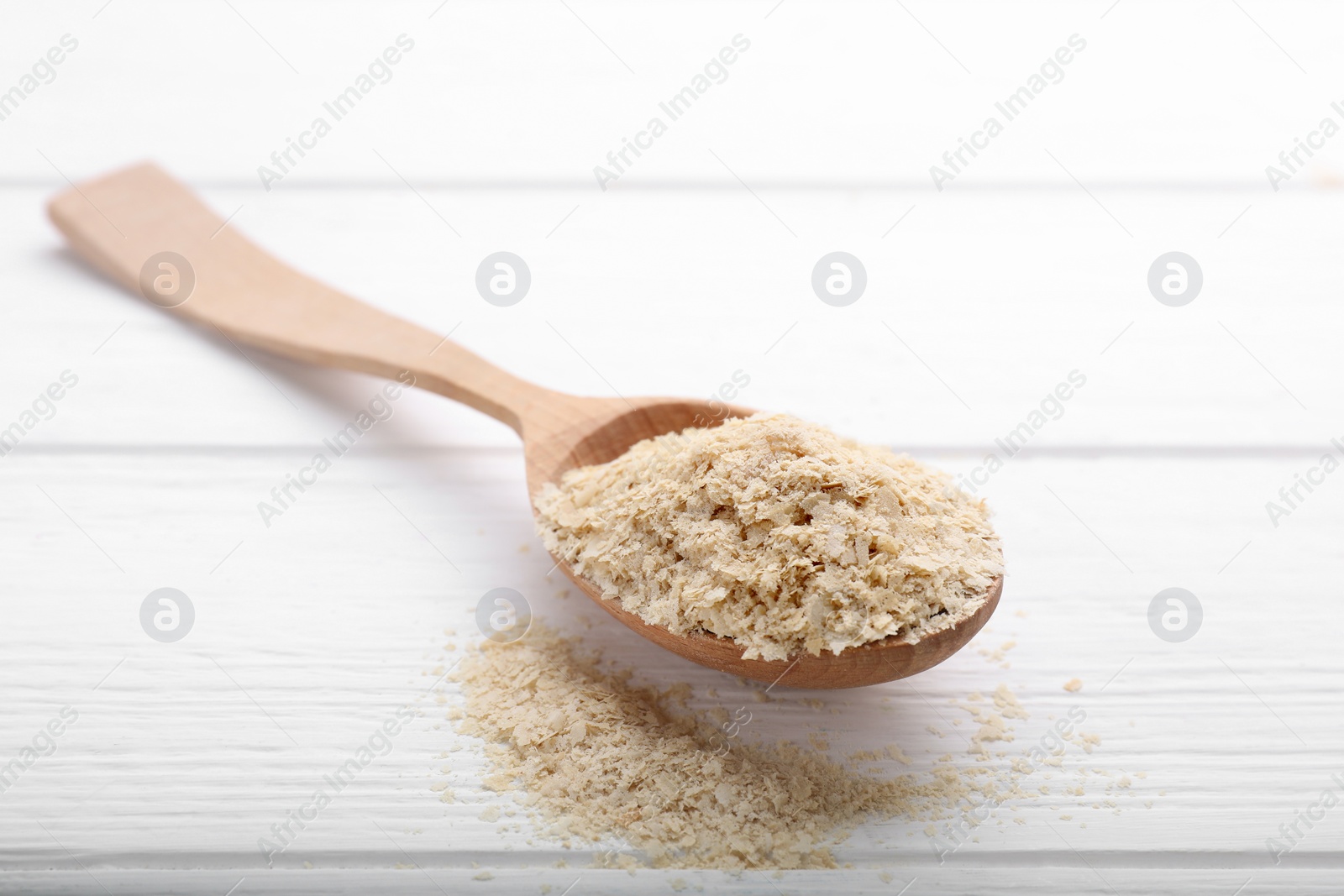 Photo of Beer yeast flakes and spoon on white wooden table, closeup