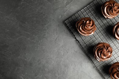 Cooling rack with delicious chocolate cupcakes on black table, top view. Space for text