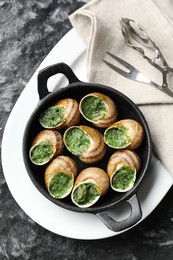 Photo of Delicious cooked snails in baking dish served on grey textured table, flat lay