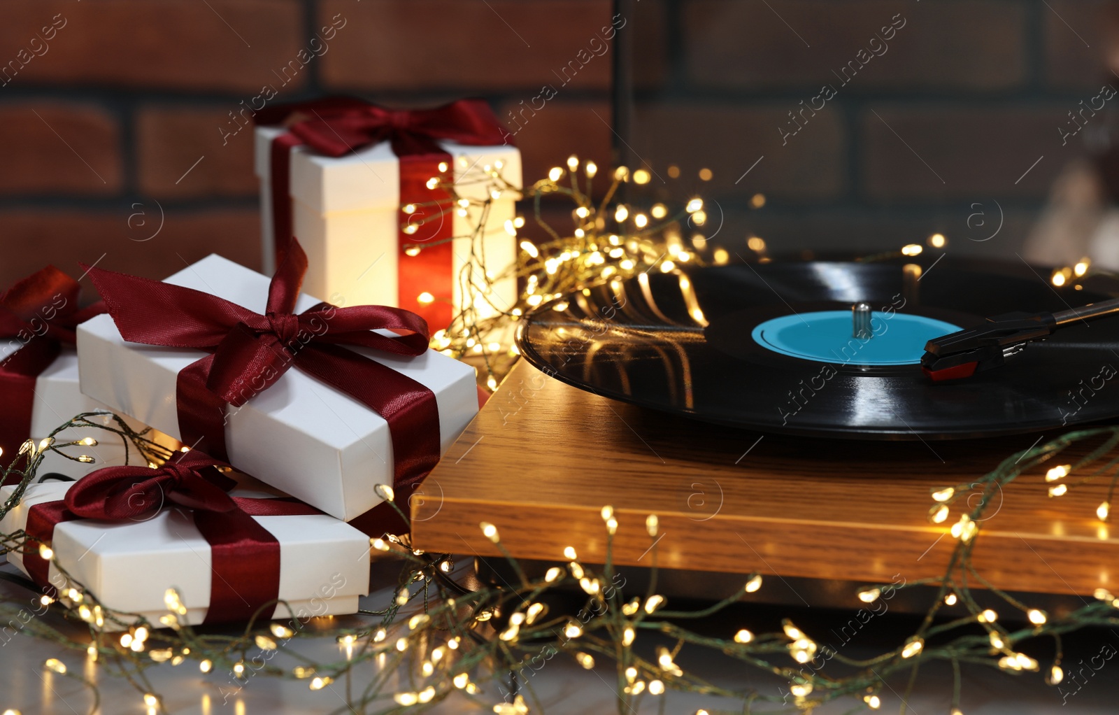 Photo of Turntable with vinyl record, fairy lights and Christmas gift boxes on grey table, closeup
