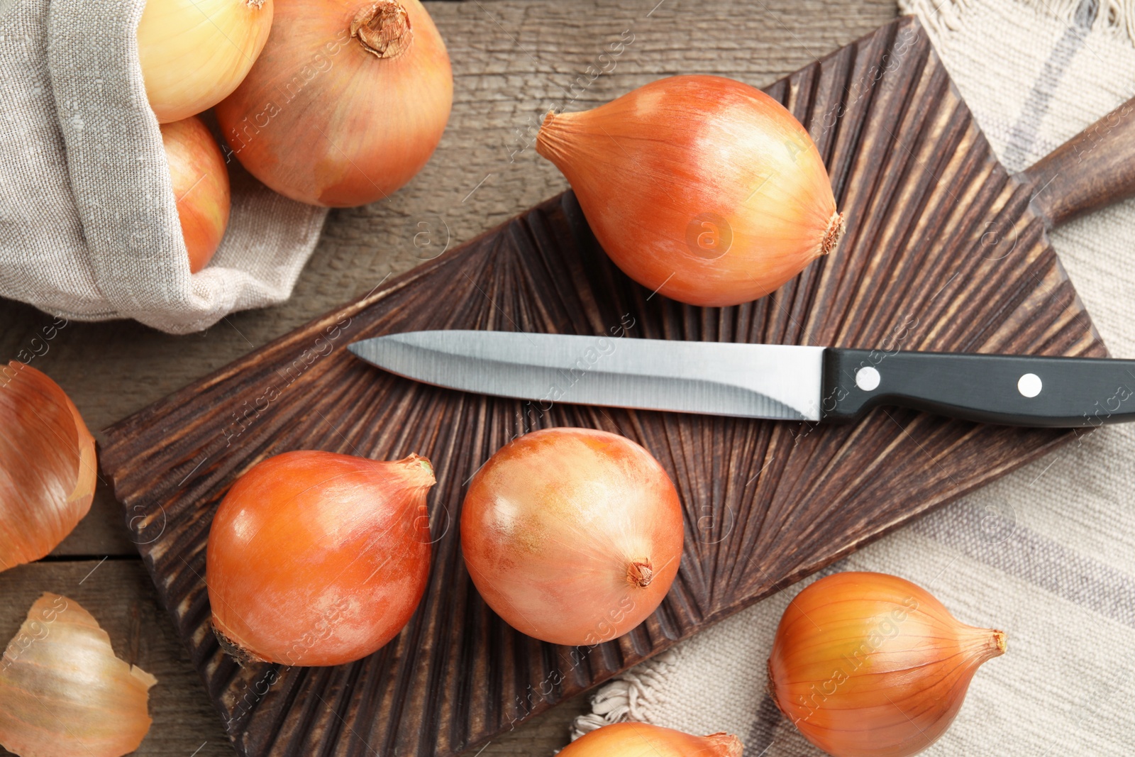 Photo of Many ripe onions and knife on wooden table, flat lay