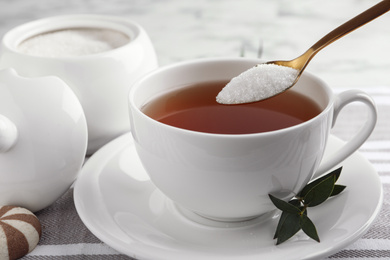 Photo of Spoon with granulated sugar over cup of tea on table