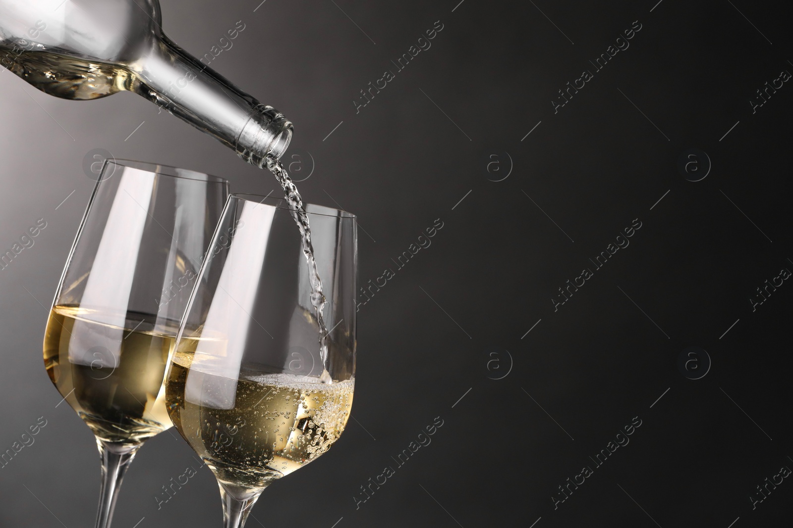 Photo of Pouring white wine into glass against grey background, closeup. Space for text