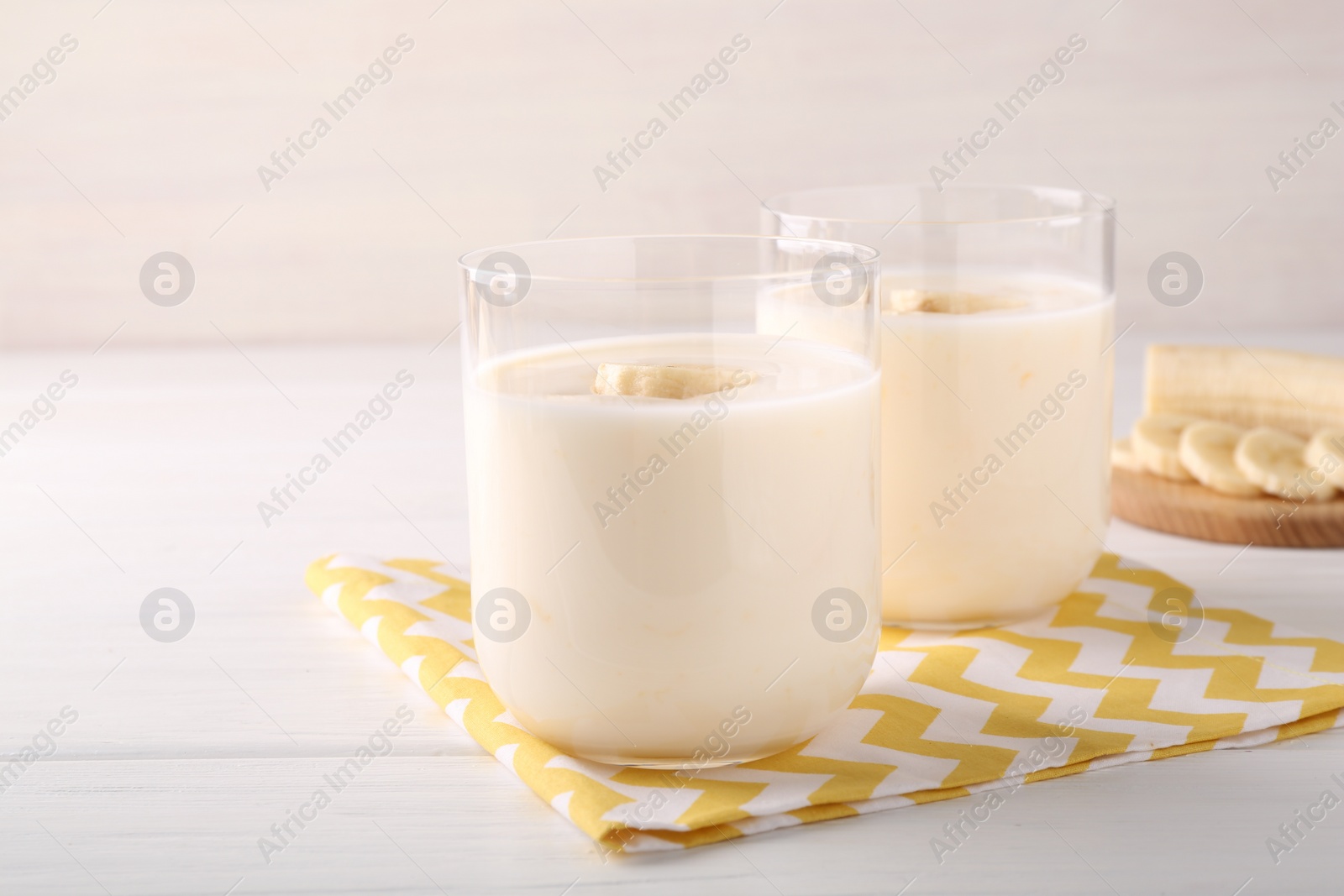 Photo of Tasty yogurt and banana in glasses on white wooden table, closeup. Space for text