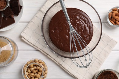 Bowl of chocolate cream, whisk, and nuts on white wooden table, flat lay