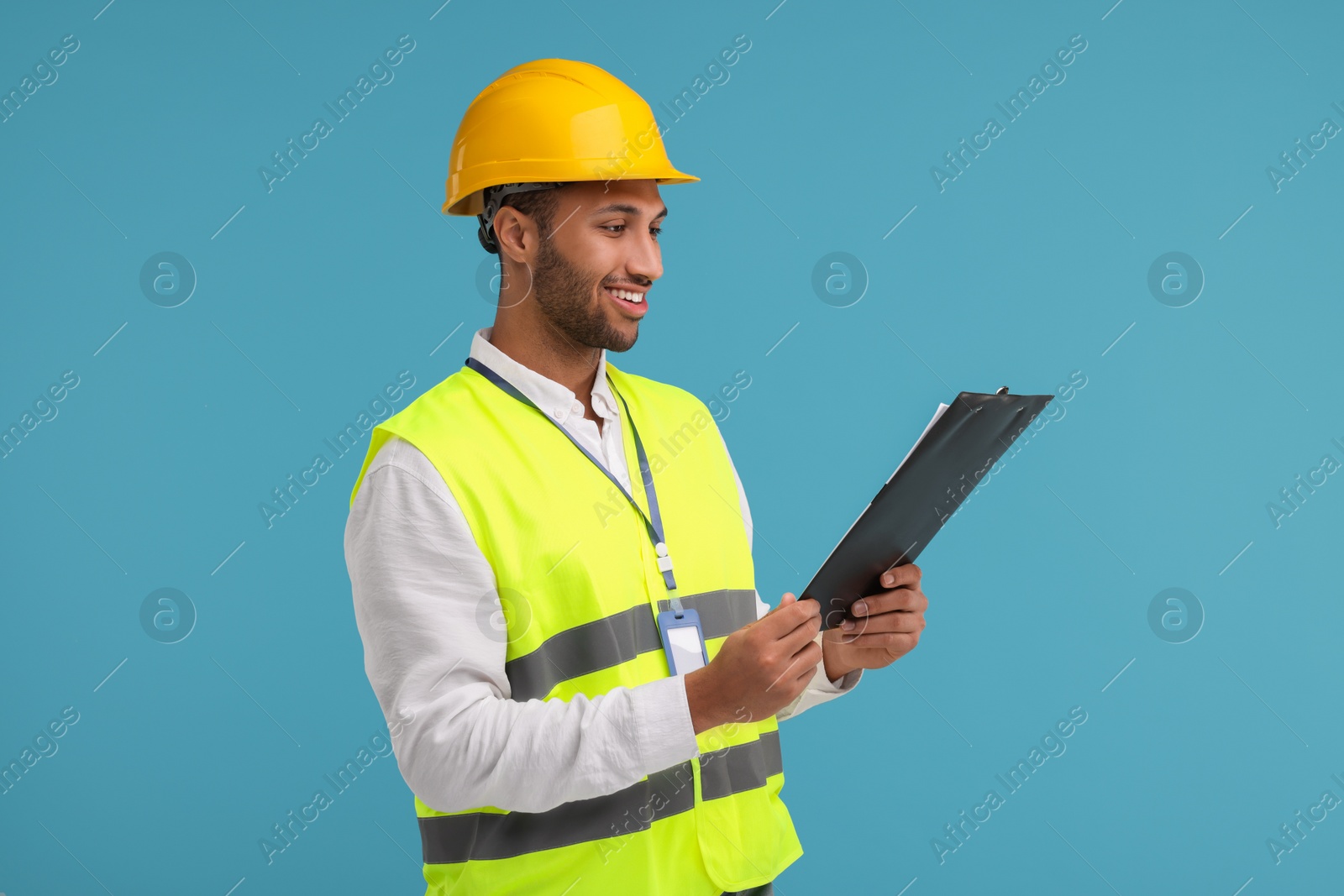 Photo of Engineer in hard hat holding clipboard on light blue background