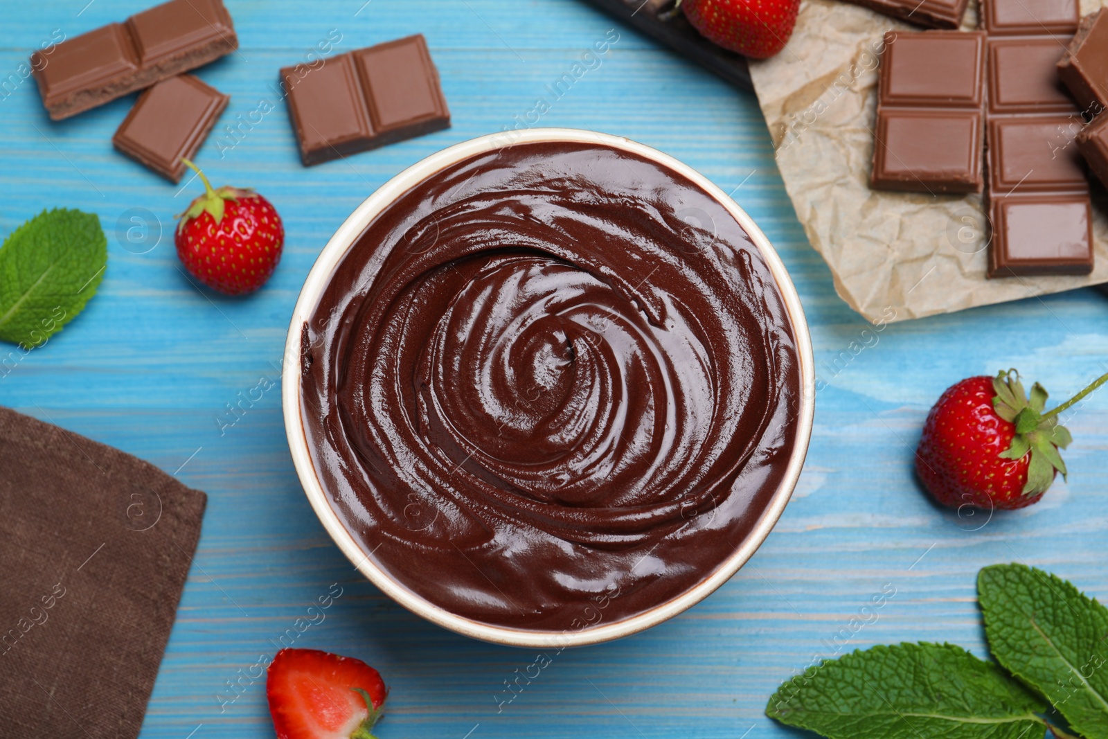 Photo of Delicious chocolate cream with strawberries and mint on light blue wooden table, flat lay