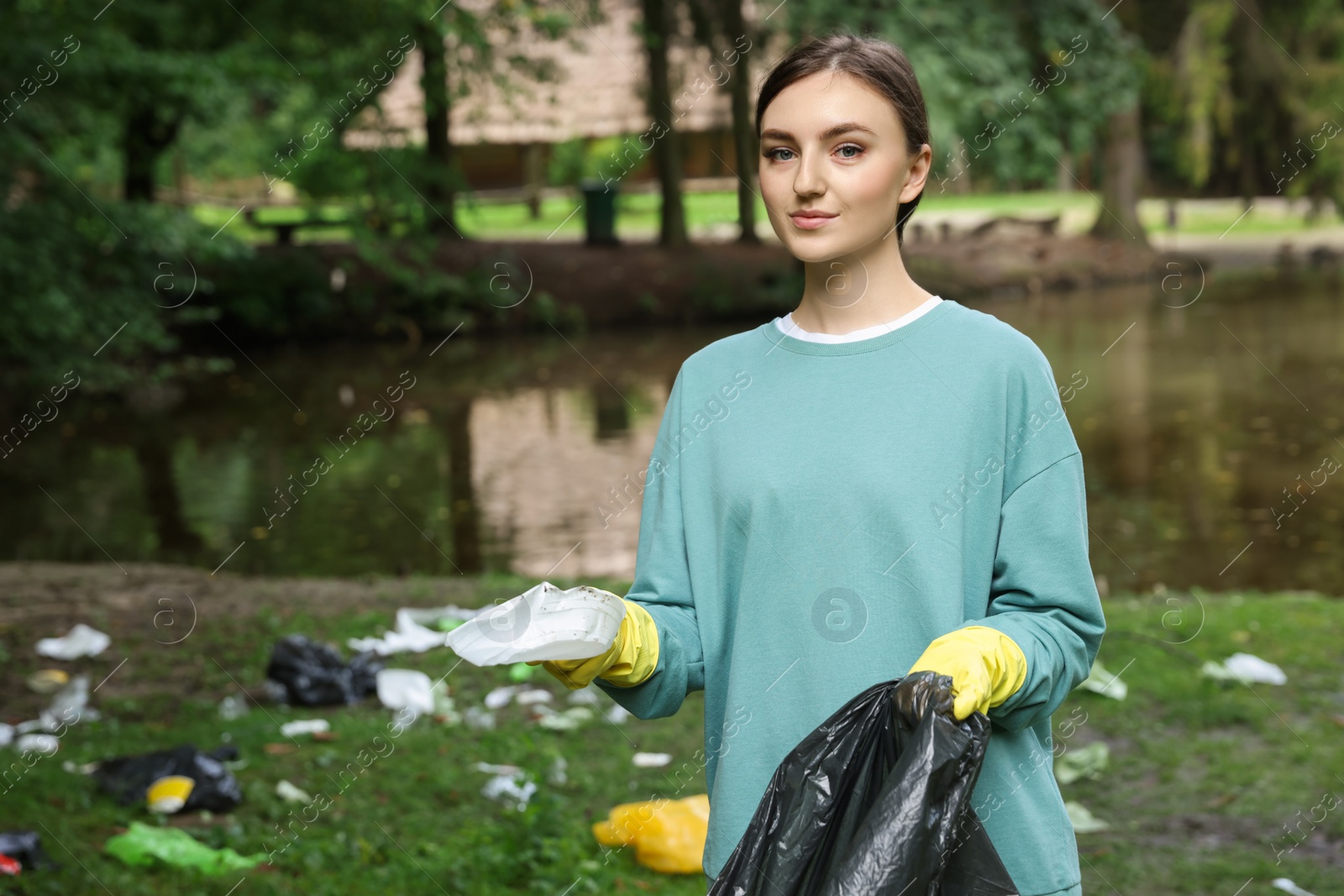 Photo of Young woman with plastic bag collecting garbage in park