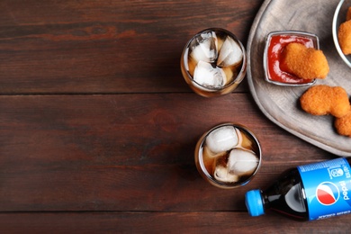 MYKOLAIV, UKRAINE - FEBRUARY 15, 2021: Glasses and bottle of Pepsi with snack on wooden table, flat lay. Space for text