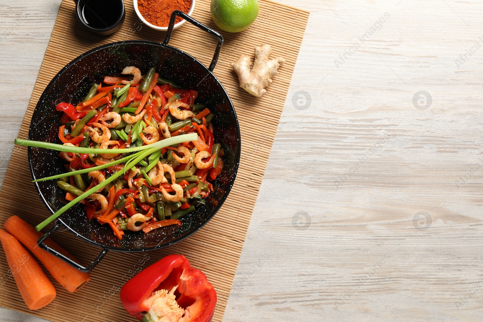 Photo of Shrimp stir fry with vegetables in wok and ingredients on wooden table, flat lay. Space for text