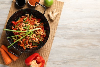 Shrimp stir fry with vegetables in wok and ingredients on wooden table, flat lay. Space for text