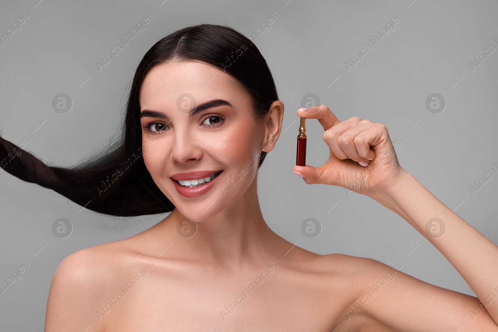 Photo of Beautiful young woman with long healthy hair holding ampoule on grey background