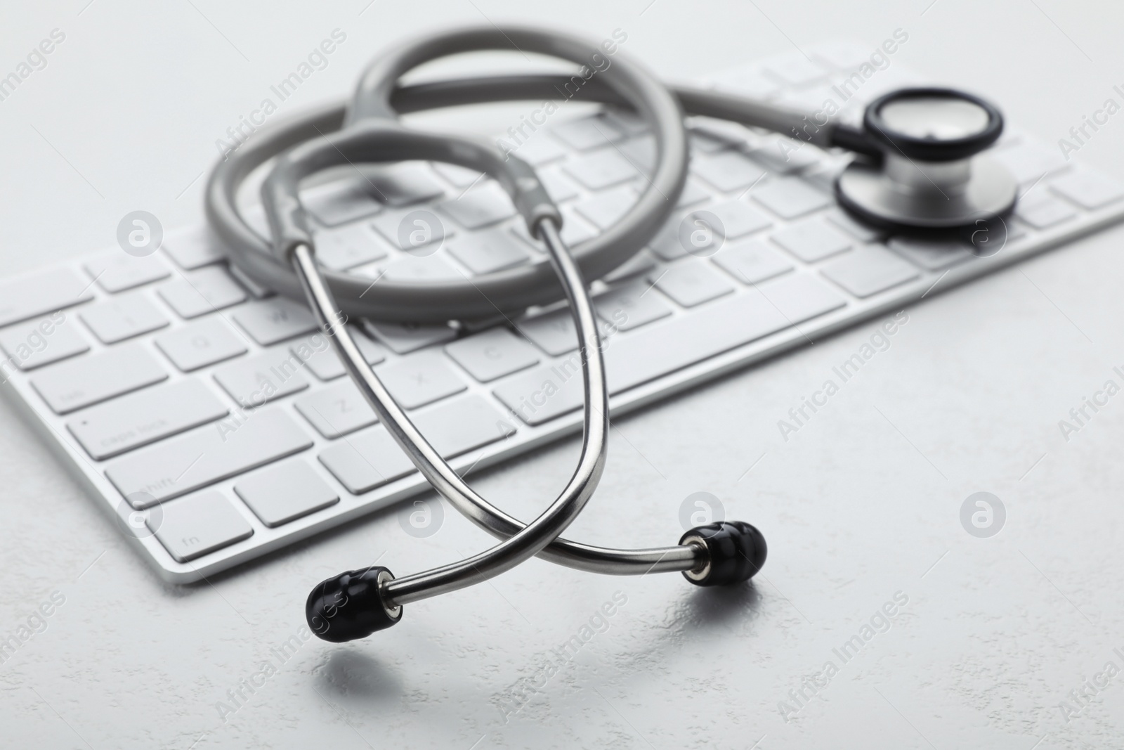 Photo of Computer keyboard with stethoscope on white table, closeup