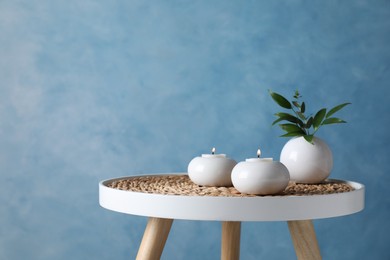 Burning candles and plant on white table against light blue background, space for text