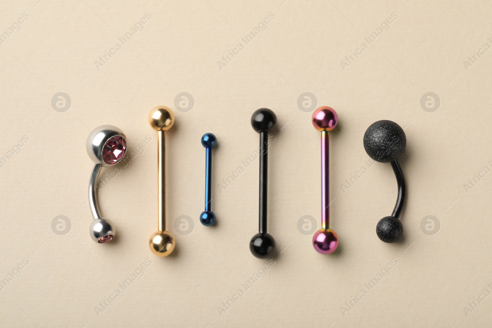 Photo of Different stylish barbells on beige background, flat lay. Piercing jewelry