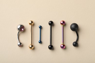 Photo of Different stylish barbells on beige background, flat lay. Piercing jewelry