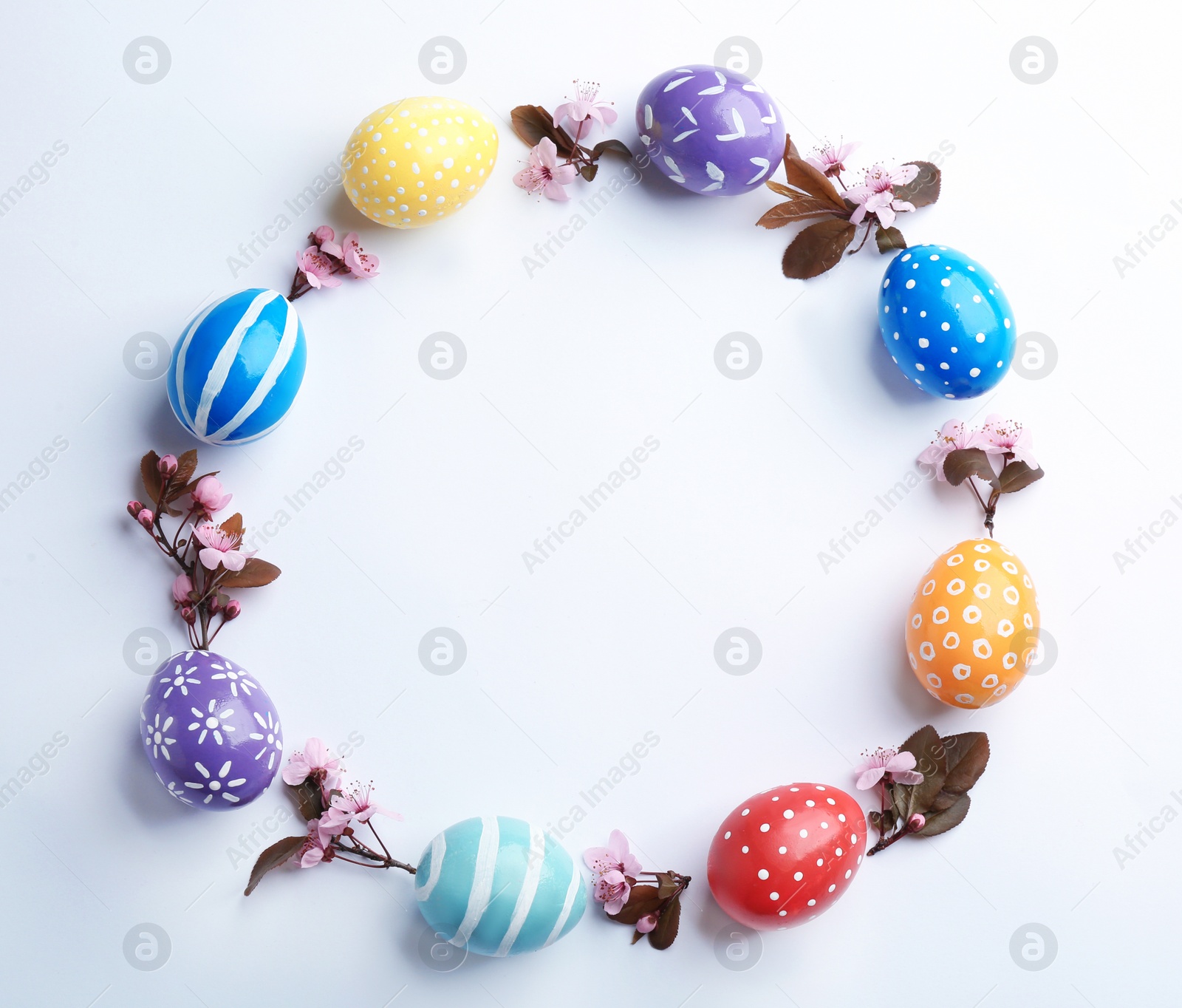 Photo of Frame made of painted Easter eggs and blossoming branches on white background, top view. Space for text