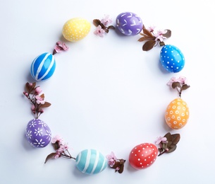 Frame made of painted Easter eggs and blossoming branches on white background, top view. Space for text