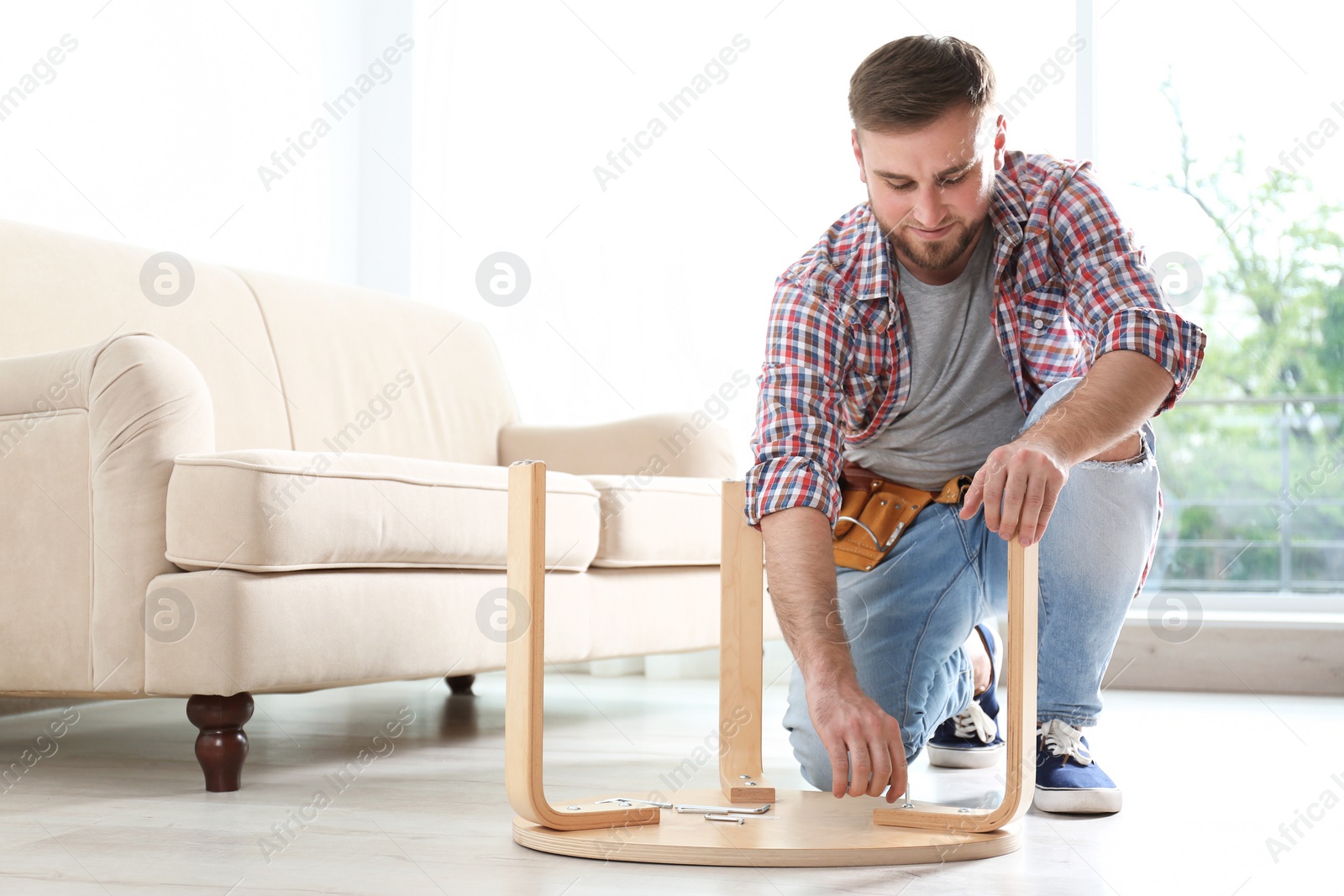 Photo of Young man working with wooden chair indoors. Space for text