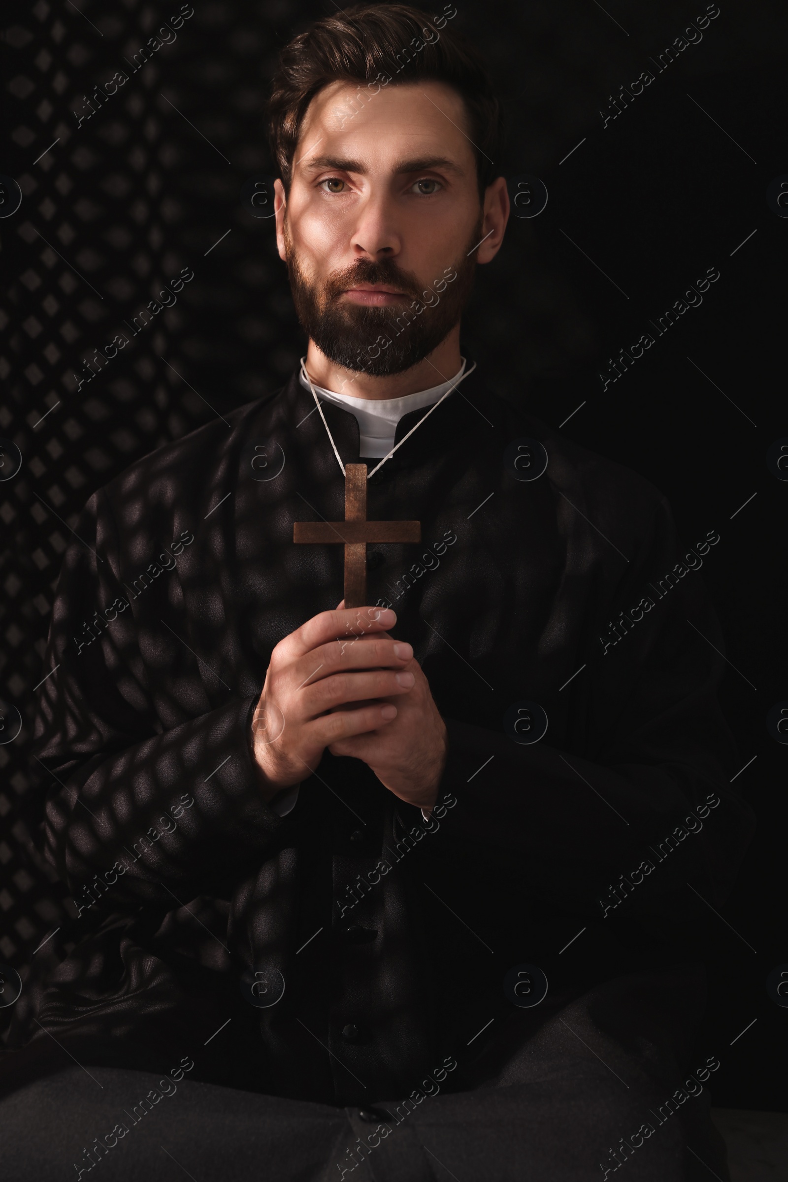 Photo of Catholic priest in cassock holding cross in confessional