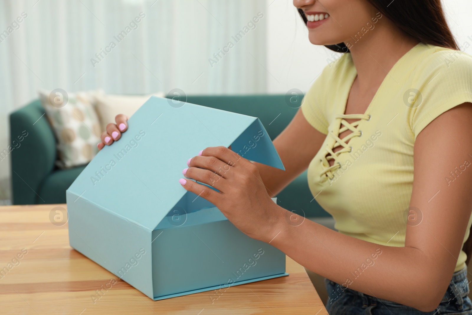 Photo of Happy young woman opening parcel at home, closeup. Internet shopping
